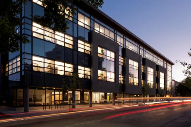 A glass-fronted commercial office building lit from within at dusk.